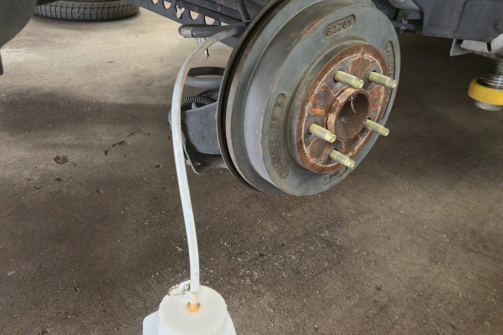 Old brake fluid draining from a rear wheel cylinder bleeder into a catch bottle during a brake fluid service