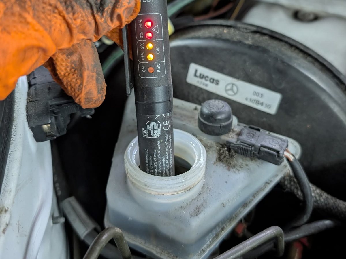 Electronic brake fluid tester dipped into a master cylinder reservoir with its LED scale lit to the top red band, indicating over 4 percent water content